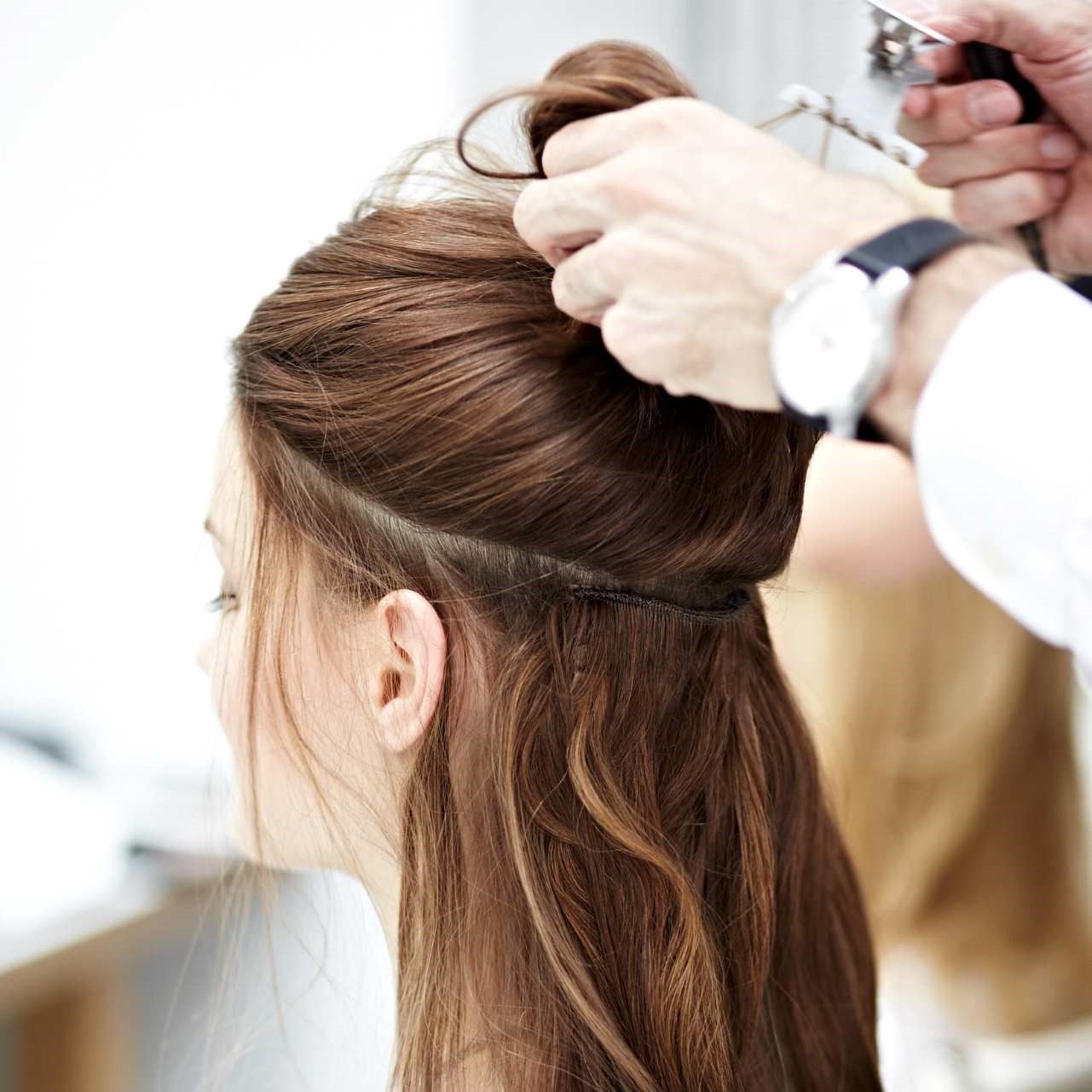 Ein Friseur hebt die oberen Haare einer Kundin hoch, um die eingearbeiteten DreamWefts-Haartressen zu zeigen.